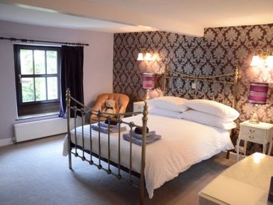 A bedroom with a metal bed frame nightstands with lamps an armchair with a teddy bear and a window at Greety Gate House in Foxfield