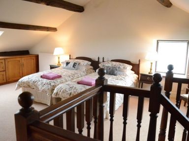 A bedroom with two single beds bedside tables lamps and wooden beams at Greety Gate House in Foxfield