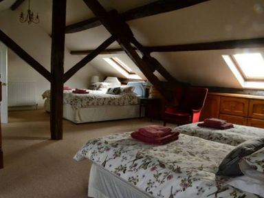 A bedroom with exposed wooden beams beds with floral bedding and folded towels a red armchair and skylight windows at Greety Gate House in Foxfield