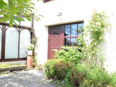 A front door with red wood frame surrounded by plants and bushes at Greety Gate House in Foxfield
