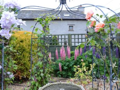 A garden with blooming flowers and a metal archway in front of a house at Greety Gate House in Foxfield