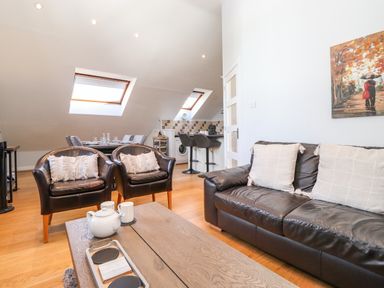 A living space with black leather sofa and chairs near a wooden coffee table and kitchen area at Sky View in Keswick