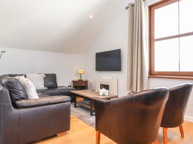 A living room with a black leather sofa black chairs wooden coffee table and wall mounted television at Sky View in Keswick