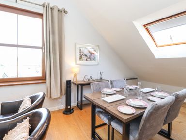A dining area with a wooden table set for six and two leather chairs near a window and skylight at Sky View in Keswick
