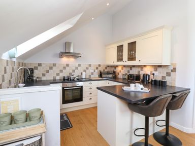 A kitchen with black countertop bar stools tiled backsplash and white cabinets at Sky View in Keswick