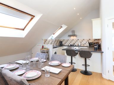 A dining table set with plates and glasses next to a kitchen with bar stools and skylight windows at Sky View in Keswick