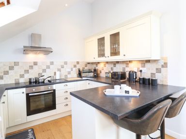 A kitchen with cream cabinets black countertop and stools at Sky View in Keswick