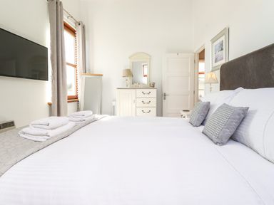 A bedroom with a bed with pillows and towels next to a dresser mirror and a wall-mounted television at Sky View in Keswick