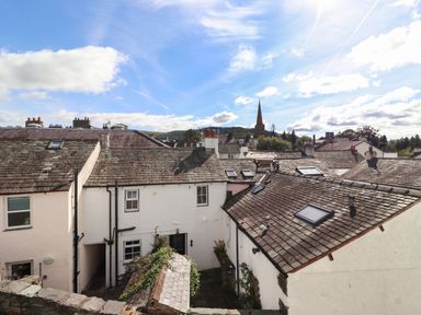 Rooftops of white buildings with chimneys and skylights under a blue sky with clouds and a distant church spire at Sky View in Keswick