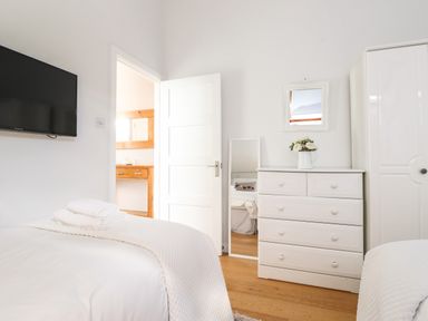 A bedroom with a white dresser a mirror flowers on the dresser a wall-mounted TV and a bed with towels on it at Sky View in Keswick