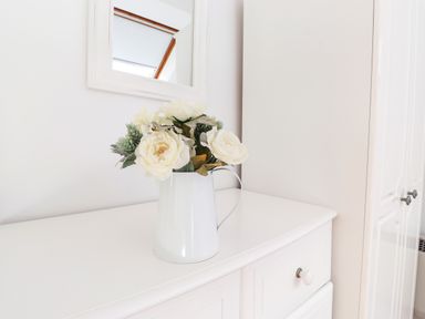 A white dresser with a white pitcher holding white flowers under a mirror in a room at Sky View in Keswick