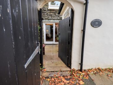 A black wooden gate entrance leading to a stone patio and glass doors with a white exterior wall showing a sign for Walkers Rest 21 at Walkers Rest in Windermere