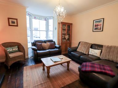 A living room with two leather sofas a wicker chair a wooden coffee table a wooden cabinet and a chandelier at Walkers Rest in Windermere
