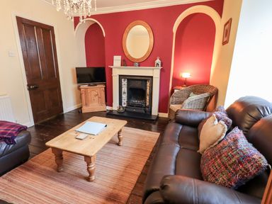 A living room with a fireplace a wooden coffee table a television a brown leather sofa and a wicker chair at Walkers Rest in Windermere
