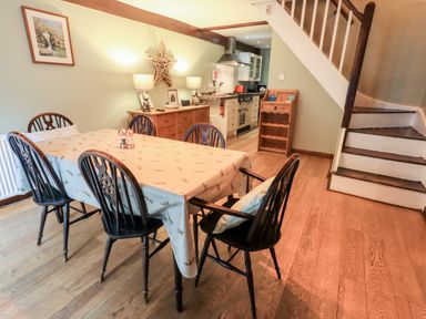 A dining room with a table and six chairs next to a wooden sideboard and staircase at Walkers Rest in Windermere