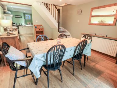 A dining room with a table covered by a cloth and six black chairs next to a staircase and kitchen at Walkers Rest in Windermere