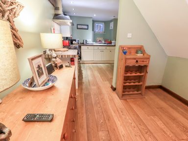 A kitchen area with wooden flooring a wooden cabinet with a lamp and framed photo a wine rack a stove and countertop in Walkers Rest in Windermere