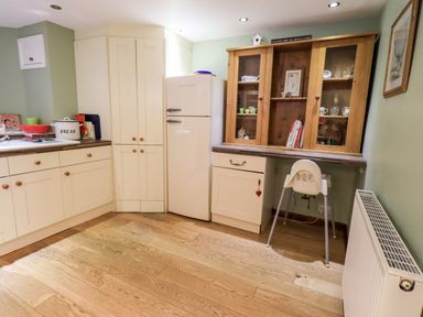 A kitchen with cream cabinets a white refrigerator wooden floor and a white high chair at Walkers Rest in Windermere