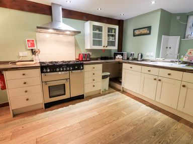 A kitchen with cream cabinets a stainless steel stove and hood and wooden flooring at Walkers Rest in Windermere