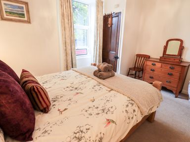 A bedroom with a bed with patterned bedding and rolled towels a wooden dresser mirror chair and window at Walkers Rest in Windermere