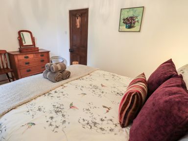 A bedroom with a bed with patterned bedding and pillows a wooden dresser with a mirror a wooden chair a door and a painting on the wall at Walkers Rest in Windermere