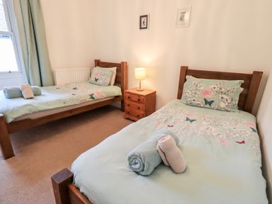 A bedroom with two single beds a wooden nightstand with a lamp and towels on the beds at Walkers Rest in Windermere