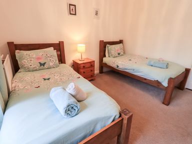 A bedroom with two single wooden beds with floral bed covers and rolled towels on each bed and a wooden nightstand with a lamp between the beds at Walkers Rest in Windermere