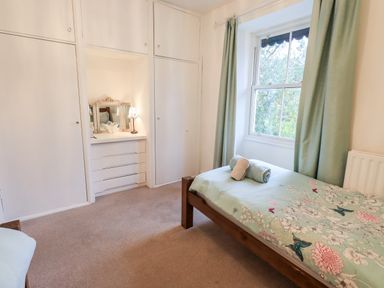 A bedroom with a single bed near a window with curtains and built in white wardrobes with a small dressing table at Walkers Rest in Windermere