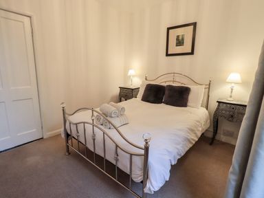 A bedroom with a metal bed frame white bedding two dark pillows folded towels on the bed two bedside tables with lamps and a framed picture on the wall at Walkers Rest in Windermere