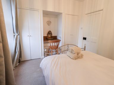 A bedroom with a metal bed frame with rolled towels on the bed a wooden chair and vanity in an alcove and two white closets at Walkers Rest in Windermere
