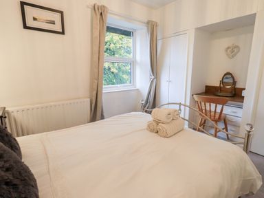 A bedroom with a bed holding rolled towels a wooden chair and desk under a window at Walkers Rest in Windermere