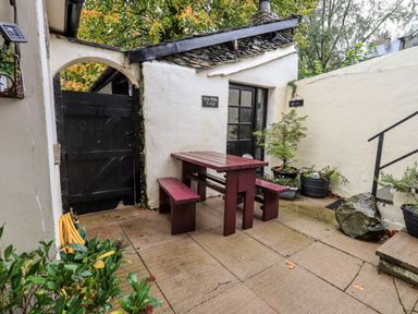 A small outdoor patio with a wooden picnic table and benches black gate potted plants and stone steps at Walkers Rest in Windermere