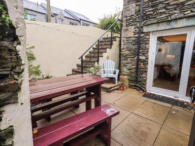 An outdoor patio with a red wooden picnic table and benches stone steps with a metal railing a white plastic chair and a glass door leading inside at Walkers Rest in Windermere