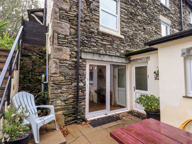 An outdoor patio area with stone walls plastic chair potted plants sliding glass door and a wooden table at Walkers Rest in Windermere