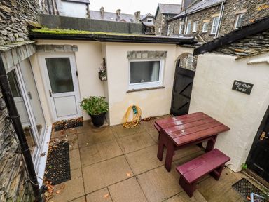 A small outdoor patio with a wooden table and bench a potted plant and a garden hose at The Olde Forge