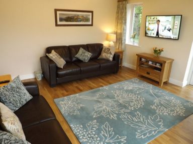 A living room with leather sofas a blue floral rug and a wall mounted television at Eribel Cottage in Threlkeld