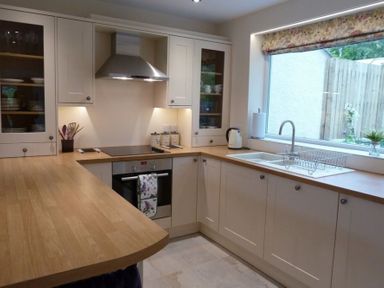A kitchen with wooden countertops white cabinets a stainless steel oven a stove a sink under a window and kitchen utensils at Eribel Cottage in Threlkeld