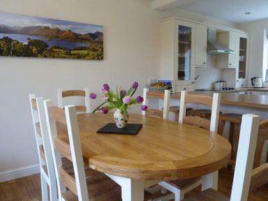 A dining area with a wooden table and chairs a vase with flowers on the table and a kitchen in the background at Eribel Cottage in Threlkeld