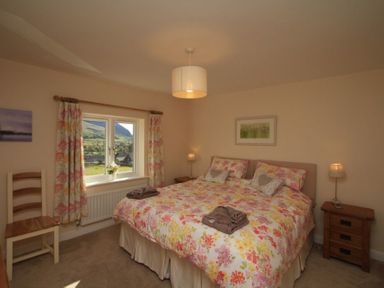 A bedroom with a double bed with floral bedding next to a window with floral curtains and a wooden chair at Eribel Cottage in Threlkeld