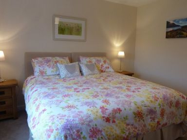 A bedroom with a double bed with floral bedspread and pillows bedside tables with lamps and wall art at Eribel Cottage in Threlkeld