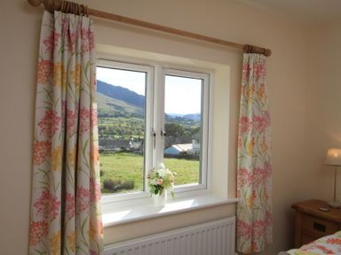 A window with floral curtains and a vase of flowers on the windowsill in a bedroom at Eribel Cottage in Threlkeld