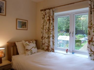 A bedroom with a single bed next to a window with curtains and garden view at Eribel Cottage in Threlkeld