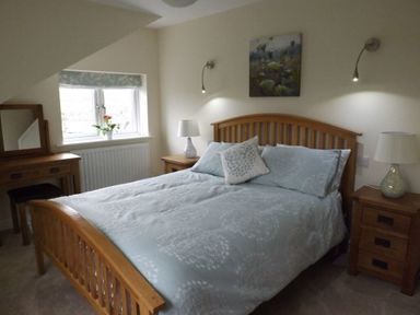 A bedroom with a wooden bed and bedside tables with lamps at Eribel Cottage in Threlkeld