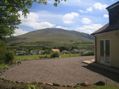 A gravel driveway with houses and a hill in the background at Eribel Cottage in Threlkeld