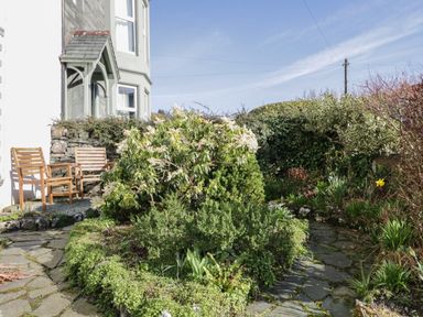A garden area with plants bushes and a stone pathway outside a house with wooden chairs at White House in Keswick