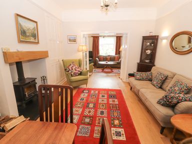 A living room and sitting area with armchairs, sofas, a wood stove, and a red patterned rug at White House in Keswick