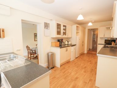 A kitchen with wooden floor cabinets countertop appliances and a dining area visible through the doorway at White House in Keswick