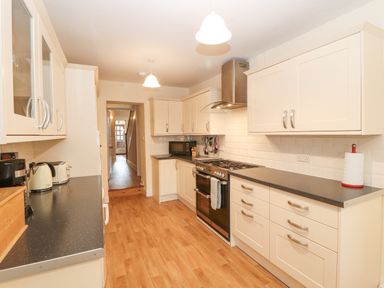 A kitchen with white cabinets black countertops a stove microwave and wooden flooring at White House in Keswick