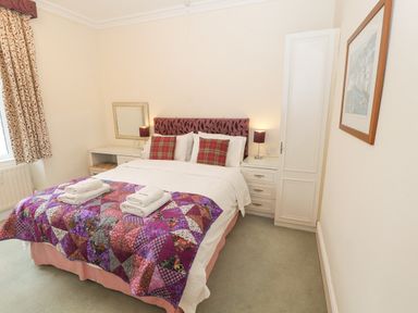 A bedroom with a double bed with purple quilt and red plaid pillows bedside tables with lamps and folded towels vanity desk with mirror framed artwork on wall at White House in Keswick
