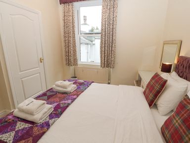 A bedroom with a bed with white bedding and plaid pillows a window with patterned curtains and a dressing table with a lamp at White House in Keswick